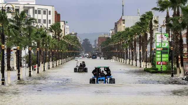 جرار زراعي كبير يحمل عددا من المواطنين ويسير وسط مياه الفيضانات في مدينة القصر الكبير وخلفه جرارات أخرى