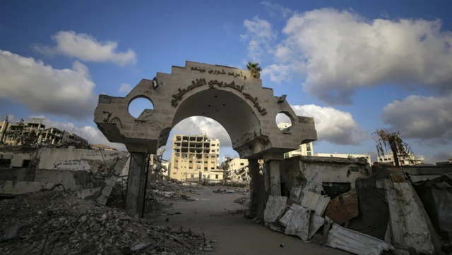 Yıkık bir kompleks giriş kapısının aralığından yıkık binalar görünüyor