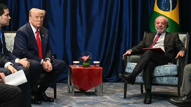 Trump e Lula sentados cada um em uma poltrona durante encontro na Malásia. 