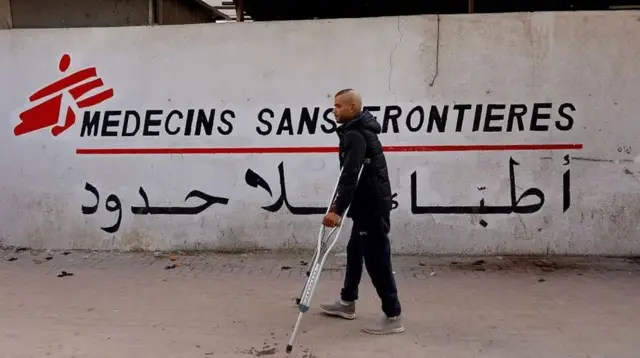 مردی با عصا در حال عبور از لوحه سازمان داکتران بدون مرز در غزه