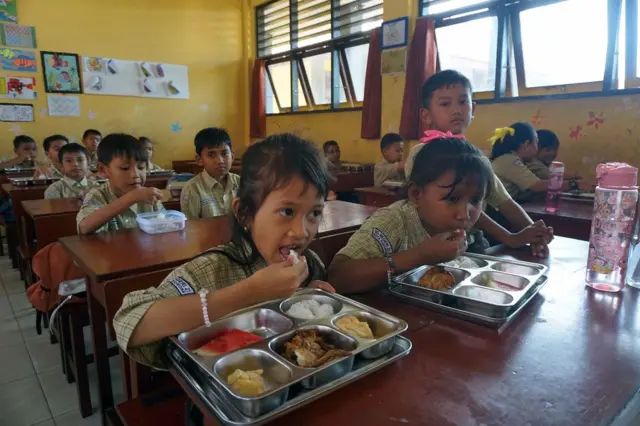 Anak-anak sedang menyantap makanan di dalam kelas.