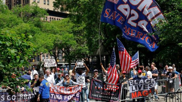 Seguidores con baderas se sitúan detrás de una valla a la espera de que llegue Trump.