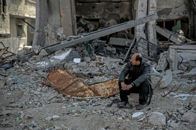 ग़ज़ा में बमबारी से तबाह हुए घर के मलबे पर बैठा एक व्यक्ति 
