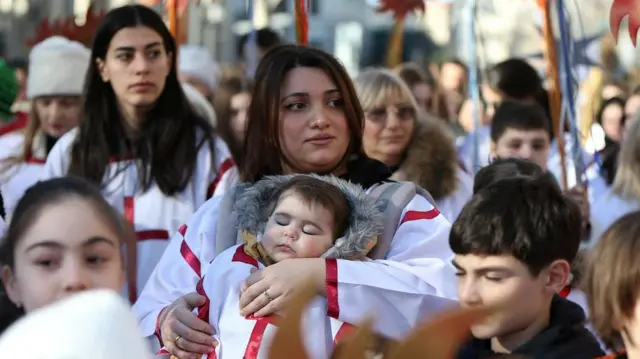 Жена у наручју држи дечака који спава у традиционалној грузијској одећи