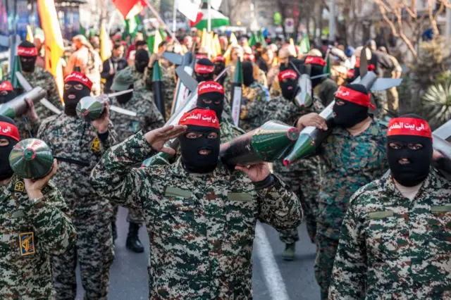 صورة أرشيفية لأحد عناصر الباسيج الملثمين يؤدون التحية للكامير ويربطون رؤوسهم بشريطة حمراء كُتب عليها 