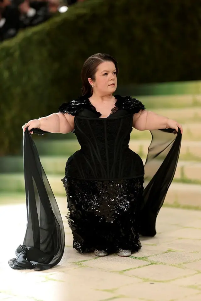 Activist, writer, and public speaker Sinéad Burke make her return to di Met Gala for black corseted gown wit flowing sleeve embellishments.