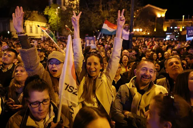 Un grupo de personas celebran en la noche de Budapest el triunfo de Peter Magyar. Llevan banderas del partido Tisza y al fondo ondea una bandera húngara.