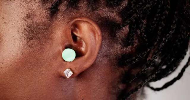 un gros plan d’une femme afro-américaine avec un bouchon d’oreille vert au travail