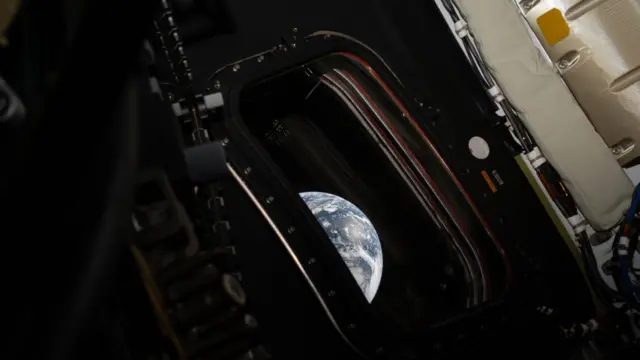 オリオン宇宙船の船内からの画像。小さな窓と、その外に見える地球が写っている。