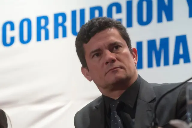 Moro com olhar sério em frente a painel em espanhol com a palavra 'corrupção'