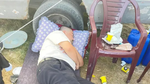 عدنان در خان یونس روی یک تشک، کنار چرخ کامیون، استراحت می‌کند