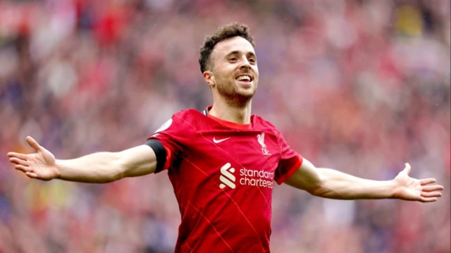 Diogo Jota, con la camiseta roja del Liverpool, sonríe con ambos brazos extendidos tras marcar un gol.
