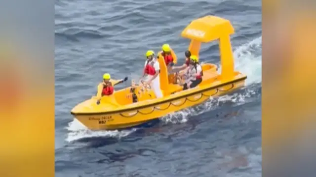 黄色い救助艇に救命胴衣と黄色いヘルメットをかぶった乗組員4人と、救助された男性と少女が乗っている。少女は乗組員の一人のひざに抱えられている