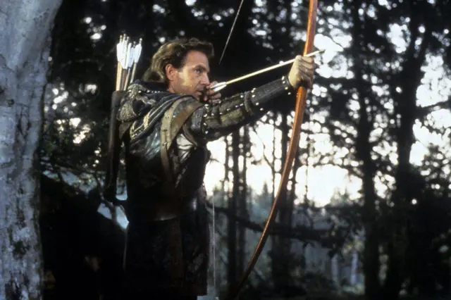 Cena do filme 'Robin Hood: O Príncipe dos Ladrões' (1991), com Kevin Costner no papel principal, preparando-se para disparar uma flecha