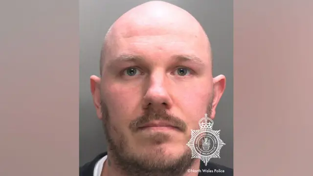 Foto policial de Miles Cross, un hombre calvo con barba y bigote. En la esquina inferior derecha de la imagen aparece el logotipo de la Policía de Gales del Norte.