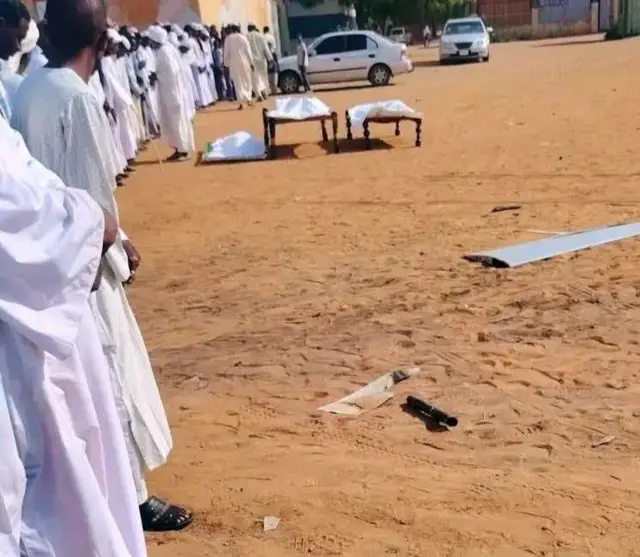 رجال يرتدون جلاليب بيضاء وعمامات وأمامهم جثث ملفوفة في وشاح أبيض.