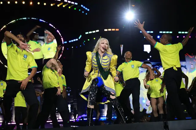 ლედი გაგა ყვითელ ქურთუკში ცეკვავს და ყვითელ მაისურებში ცეკვავს