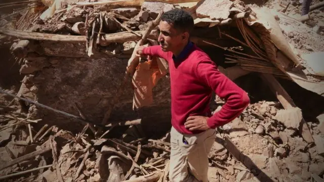 Ed-Abdullah se tient dans les décombres de son ancienne maison, appuyé sur une pile de débris.