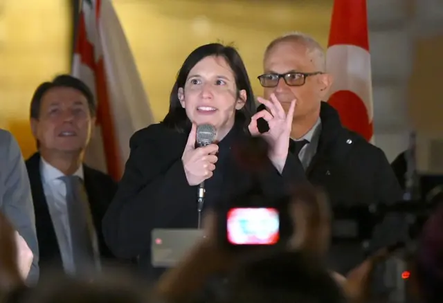 Kumral bir kadın, elinde mikrofon, konuşma yapıyor.