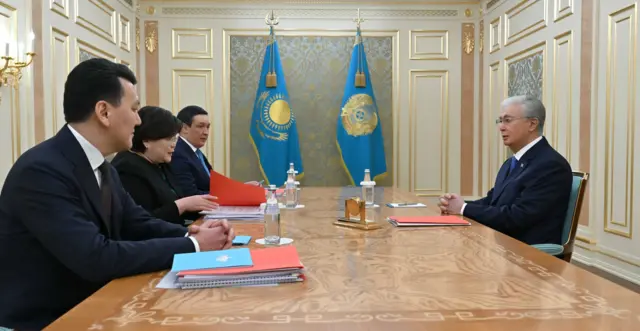 Токаев в темно-синем костюме сидит за столом, а напротив него трое членов Конституционной комиссии