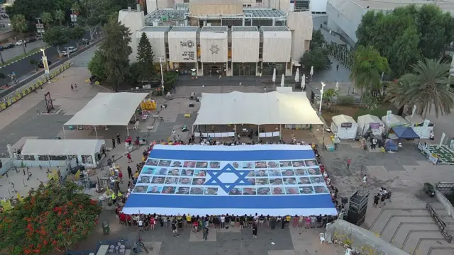 Демонстранттар барымтадагылардын сүрөттөрү түшүрүлгөн Израилдин желегин Тель-Авивдеги “Туткундар аянтына” жайып алышты