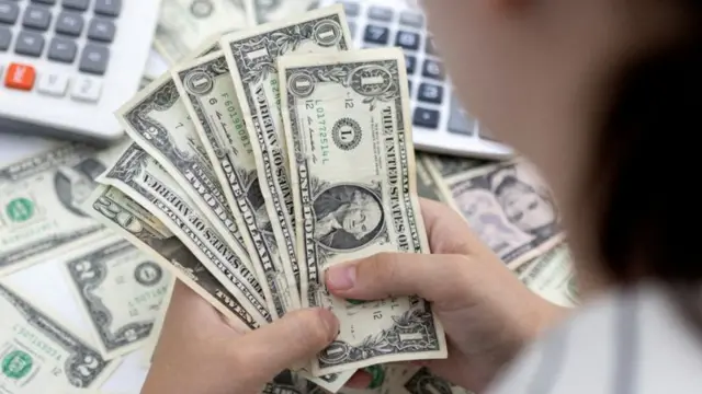 Mulher manuseando notas de dólar com calculadora ao fundo