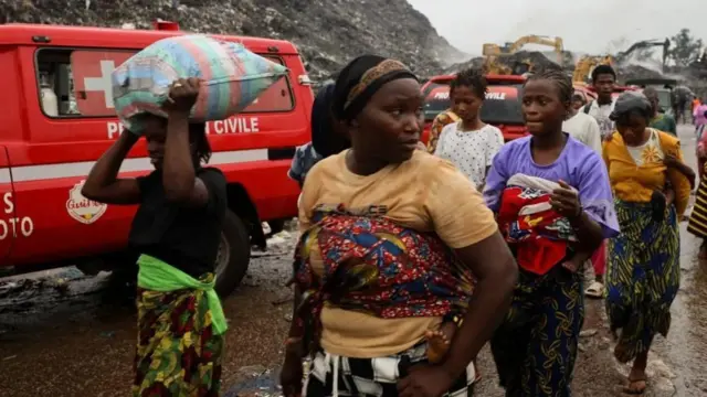 Akitan kan ga gogoro ninu aworan yii, bẹẹ ni awọn obinrin kan n fi ẹṣẹ rin lọ, awọn kan pọn ọmọ sẹyin ninu wọn, bẹẹ ni ẹnikan gbe apo ru sori.
Ẹrọ katkata wa lẹyin, bẹẹ ni ọkọ pupa kan naa wa nibẹ pẹlu.