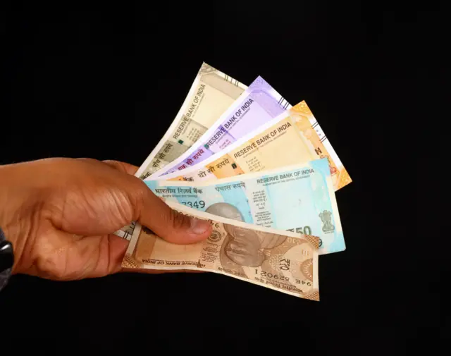 Une main tenant une collection colorée de divers billets indiens isolés sur un fond sombre.