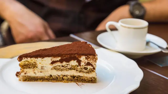 O porție de tiramisu pe o farfurie albă, cu o ceașcă de cafea lângă