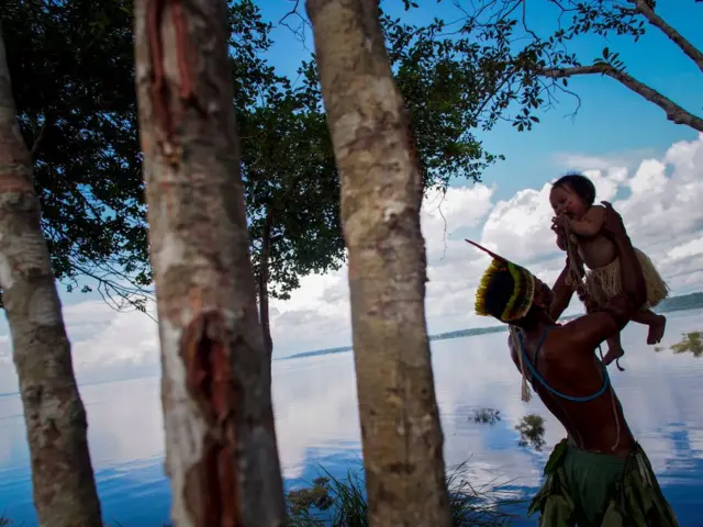  Um homem indígena Dessana brinca com um bebê próximo ao Rio Negro na Reserva Tupe nos arredorescbet jetManaus, Amazonas