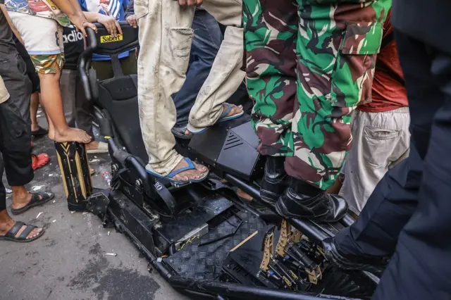 Kaki masyarakat dan lars TNI sedang berdiri di atas miniatur kendaraan.