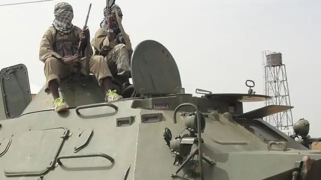Two masked man stand onotp armoured tank wit guns