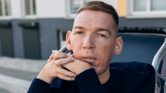 Назарій Гусаков у кріслі, біля великої будівлі