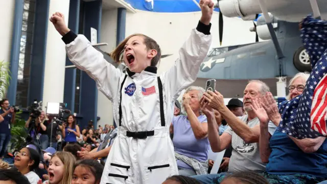 Dečak u astronomskom odelu u masi podignutih ruku dočekuje sletanje posade Artemis Dva