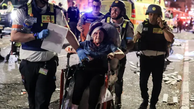 İsrailli acil durum görevlileri, Tel Aviv yakınlarındaki Ramat Gan'a düzenlenen füze saldırısında yaralanan bir kadını tekerlekli sandalyede taşırken.