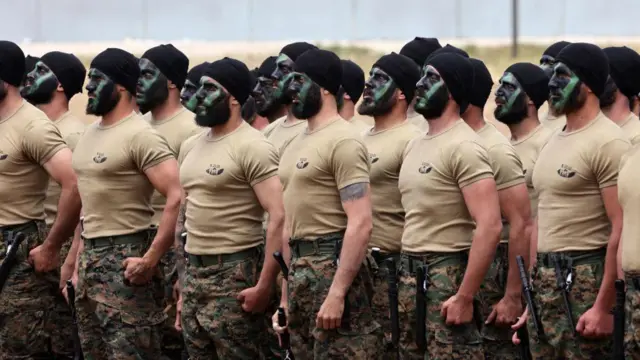 Membros do Hezbollah com rostos pintados para camuflagem enfileirados.