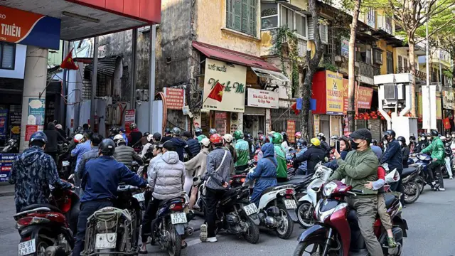 Crowds of people on motorcycles waiting on the road outside a petrol station, with the photo taken from the back of the queue.