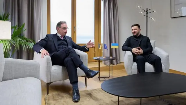 グレーを基調としたモダンな部屋で、デウェーヴェル首相とゼレンスキー大統領が座って会談している。2人の間にあるコーヒーテーブルには、ベルギーとウクライナの国旗と、そしてEUの旗のミニチュアが置かれている