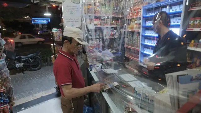 مردی در یک مغازه در تهران با کارت بانکی پول پرداخت می‌کند