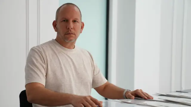 Мужчина в светлой футболке сидит за столом 