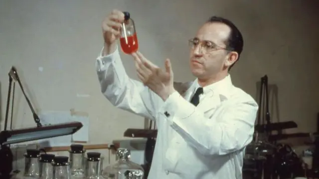 El dr. Salk con un frasco en la mano con una sustancia roja