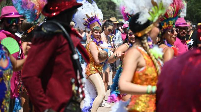 A dancer from a carnival samba band breastfeeds as they parade through the festival site on Day 4 of Glastonbury Festival 2023 on 24 June 2023 in Glastonbury, United Kingdom. 