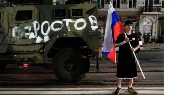 Un homme pose avec le drapeau russe devant un véhicule de l'armée