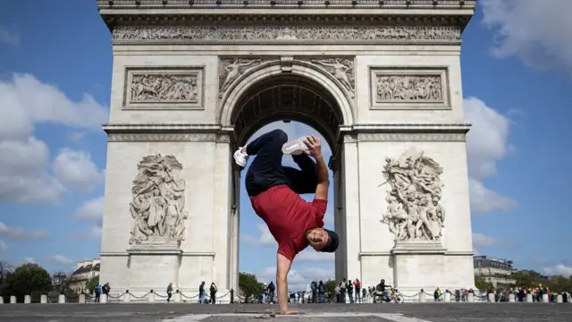 Um jovem, equilibrado sobre uma mão diante do Arco do Triunfo