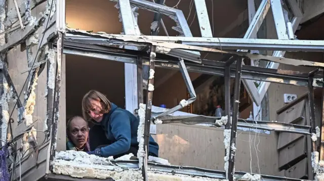 युक्रेनमा युद्धबाट क्षतिग्रस्त भवनमा मानिसहरू
