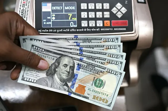 Un travailleur tenant des billets de banque en dollars américains pose pour une photo dans un bureau de change à New Delhi, le 31 juillet 2025. 