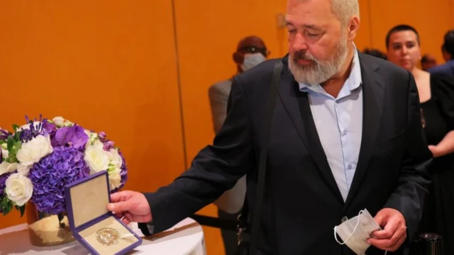 Dmitry Muratov en costard tient à l'aide de l'une de ses mains une médaille rangée dans une boîte violette