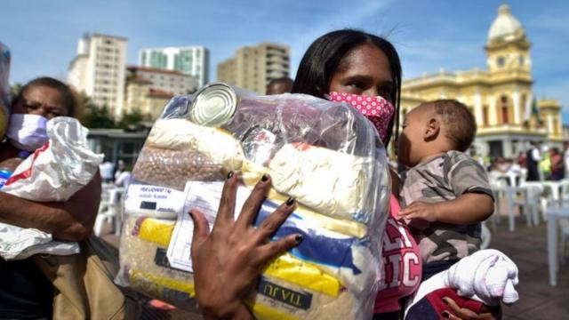 Mulher com criança no colo recebendo doaçãocasino room onlinecesta básica durante a pandemia