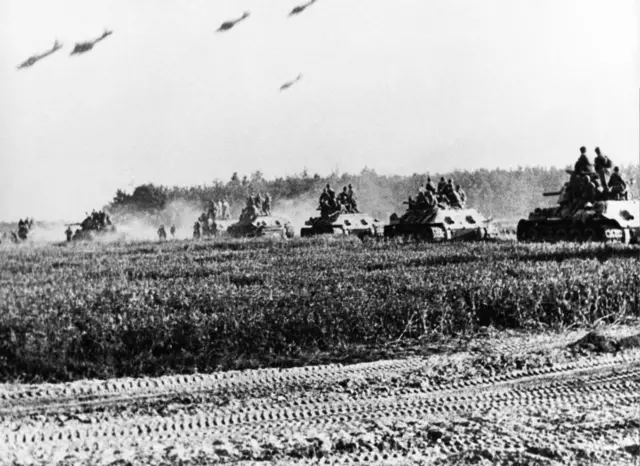 imagem histórica em preto e branco mostra sequencia de tanques avançando sob campo