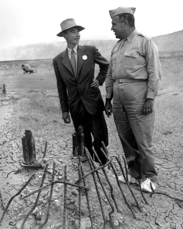 Robert Oppenheimer analisando com o general Leslie Groves os restos da torre de aço após o teste Trinity em foto em preto e branco